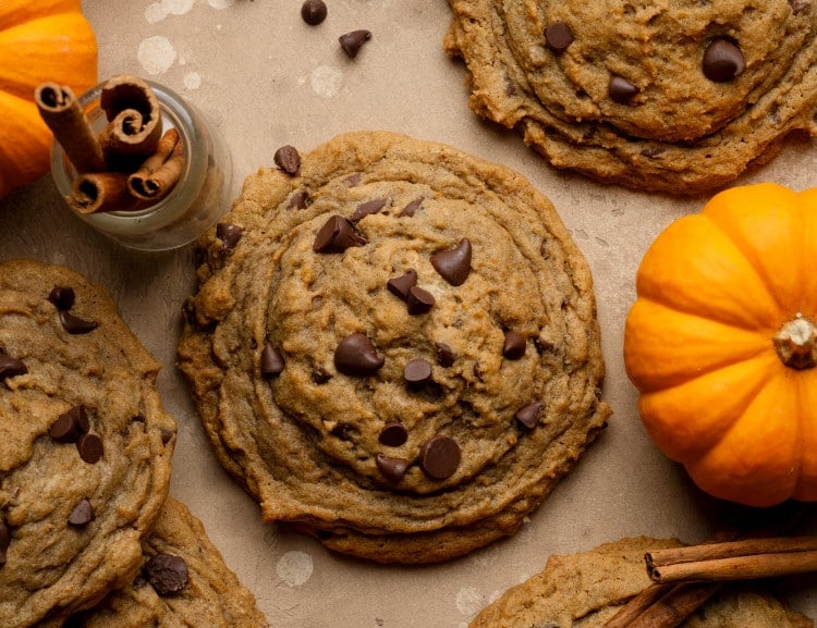 Pumpkin chocolate chip cookies topped with extra chocolate chips on parchment paper.