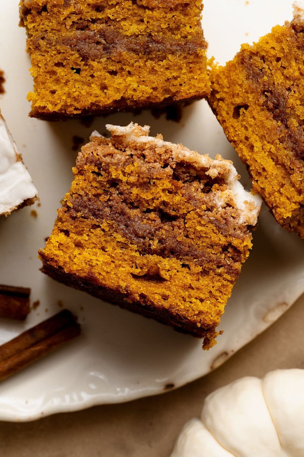 Top view of pumpkin coffee cake slices on a white plate, showing the cinnamon swirl layers and glaze on top. Cinnamon sticks and mini pumpkins are styled around the plate.