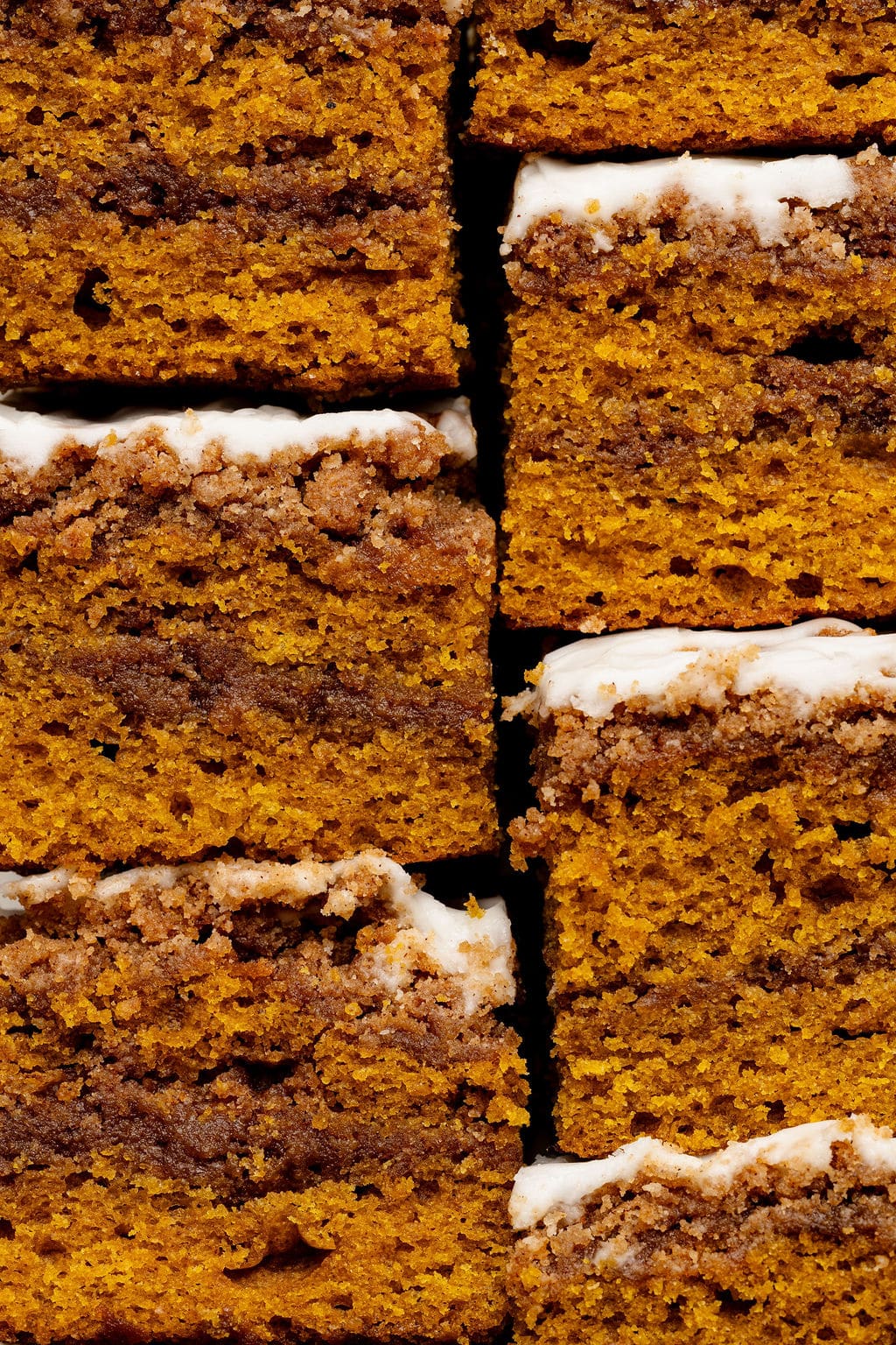 Stacked squares of pumpkin coffee cake, highlighting the thick layers of spiced pumpkin cake, cinnamon swirl, and white glaze on top.