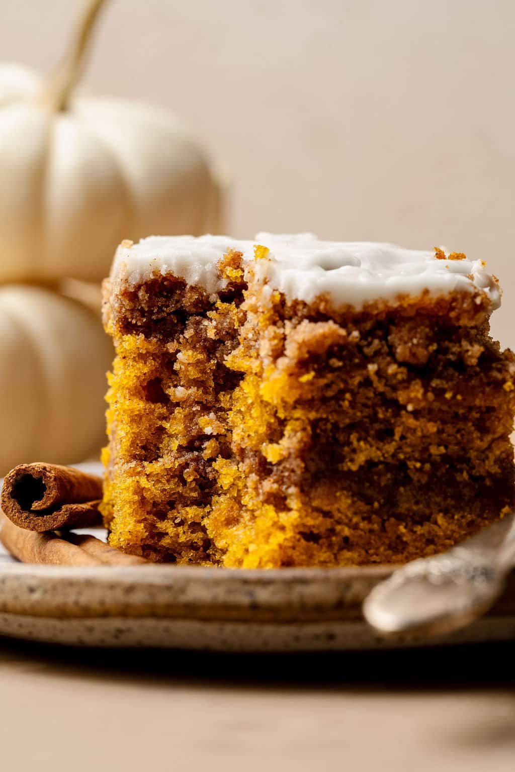 Close-up of a slice of pumpkin coffee cake with visible layers of cinnamon swirl and glaze, served on a speckled plate with a fork.