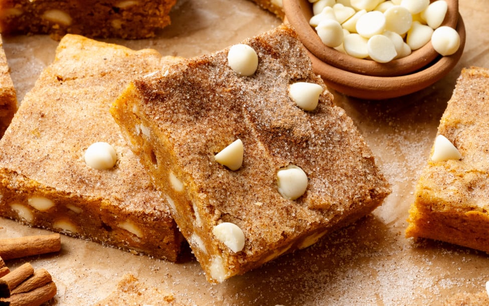 Pumpkin snickerdoodle blondies cut into squares on parchment paper lined table.