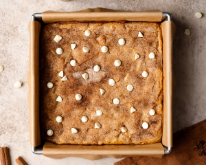 Pumpkin snickerdoodle blondies baked in an 8x8-inch pan and garnished with extra white chocolate chips after removing from the oven.
