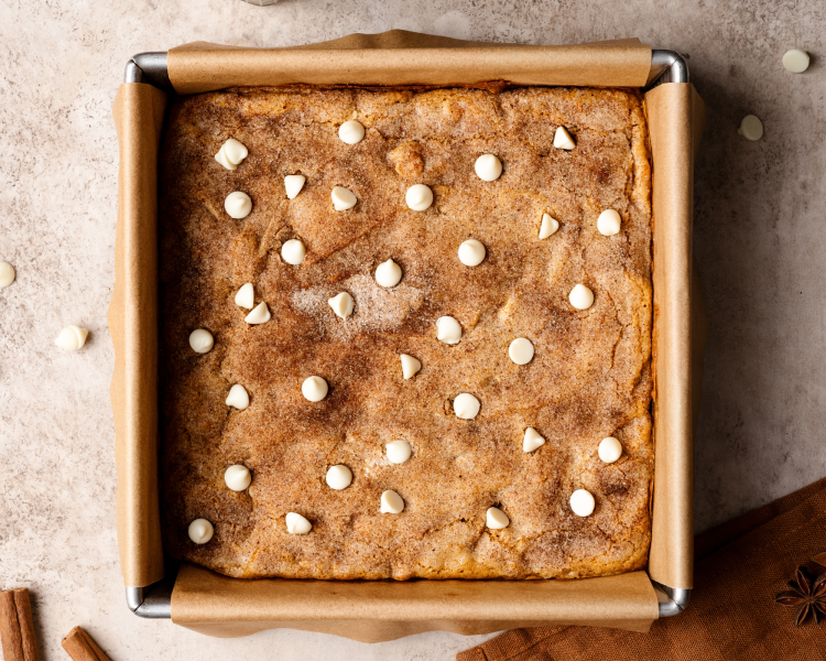 Pumpkin snickerdoodle blondies baked in an 8x8-inch pan and garnished with extra white chocolate chips after removing from the oven.