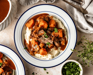Pot roast on top of mashed potatoes in white serving bowl.