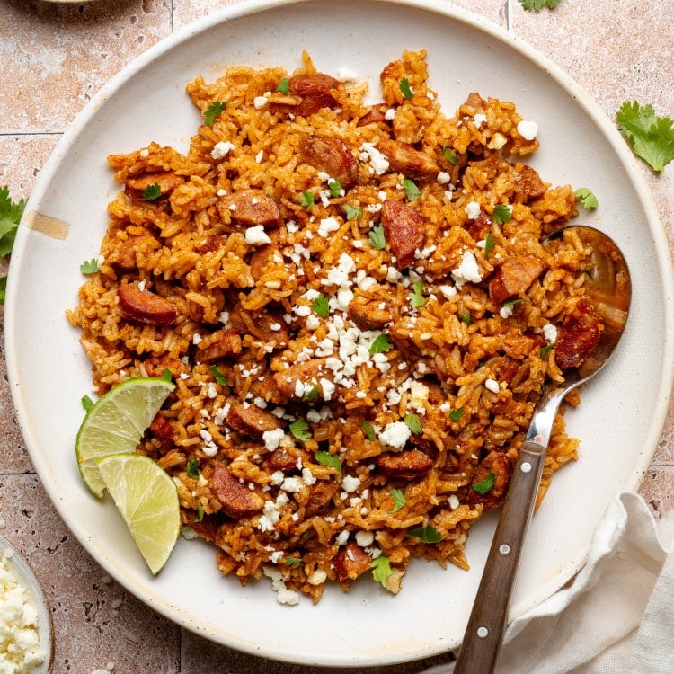 Spanish rice and chorizo on plate garnished with lime wedges and spoon on side of plate.