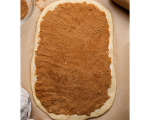 Overhead image of rolled-out cinnamon roll dough spread evenly with a thick layer of brown sugar and cinnamon filling, ready to be rolled into logs.