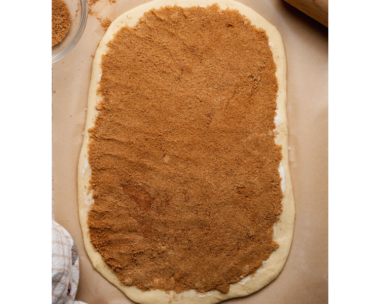 Overhead image of rolled-out cinnamon roll dough spread evenly with a thick layer of brown sugar and cinnamon filling, ready to be rolled into logs.