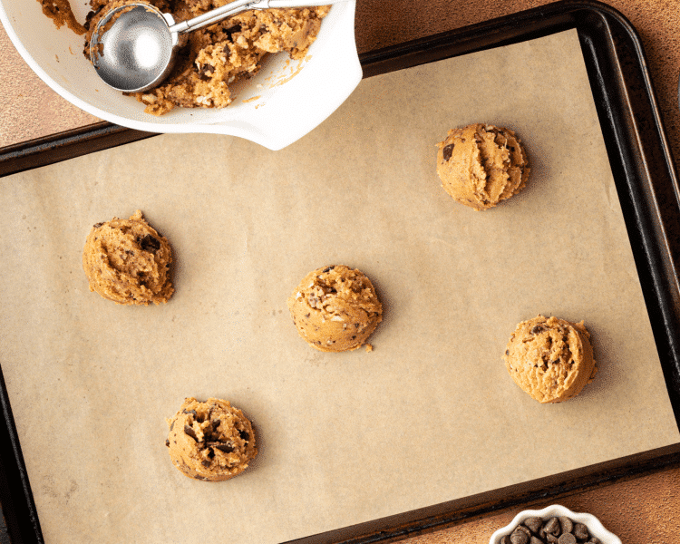 Brown butter pecan cookie dough scooped onto parchment-lined baking sheet.