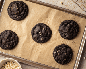Five black and white cookies baked on parchment-lined baking sheet.