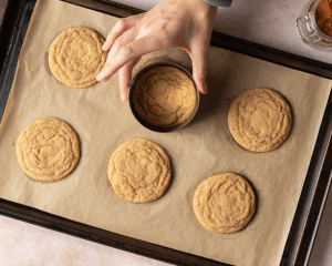 Using a cookie cutter to make cookies perfectly circular after baking on parchment-lined baking tray.