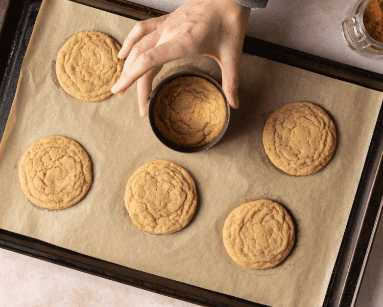 Using a cookie cutter to make cookies perfectly circular after baking on parchment-lined baking tray.