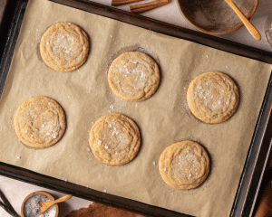 Six brown sugar cookies baked and sprinkled with flaky sea salt on parchment-lined baking tray.