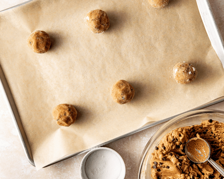 Rolling the dough balls in granulated sugar and placing on baking sheet lined with parchment paper.