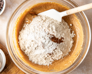 Adding the dry ingredients to the wet ingredients in the mixing bowl.