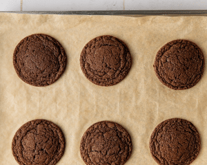 Six baked chocolate cookies on parchment lined baking sheet.
