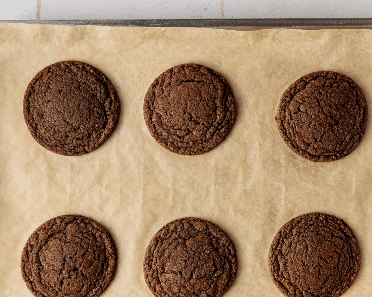 Six baked chocolate cookies on parchment lined baking sheet.