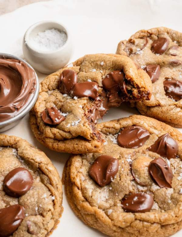Nutella stuffed chocolate chip cookies on plate with a bite taken out of one of the cookies to show the center.