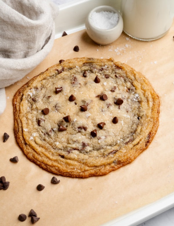 Giant single-serve thin and chewy cookie on baking tray lined with parchment paper.