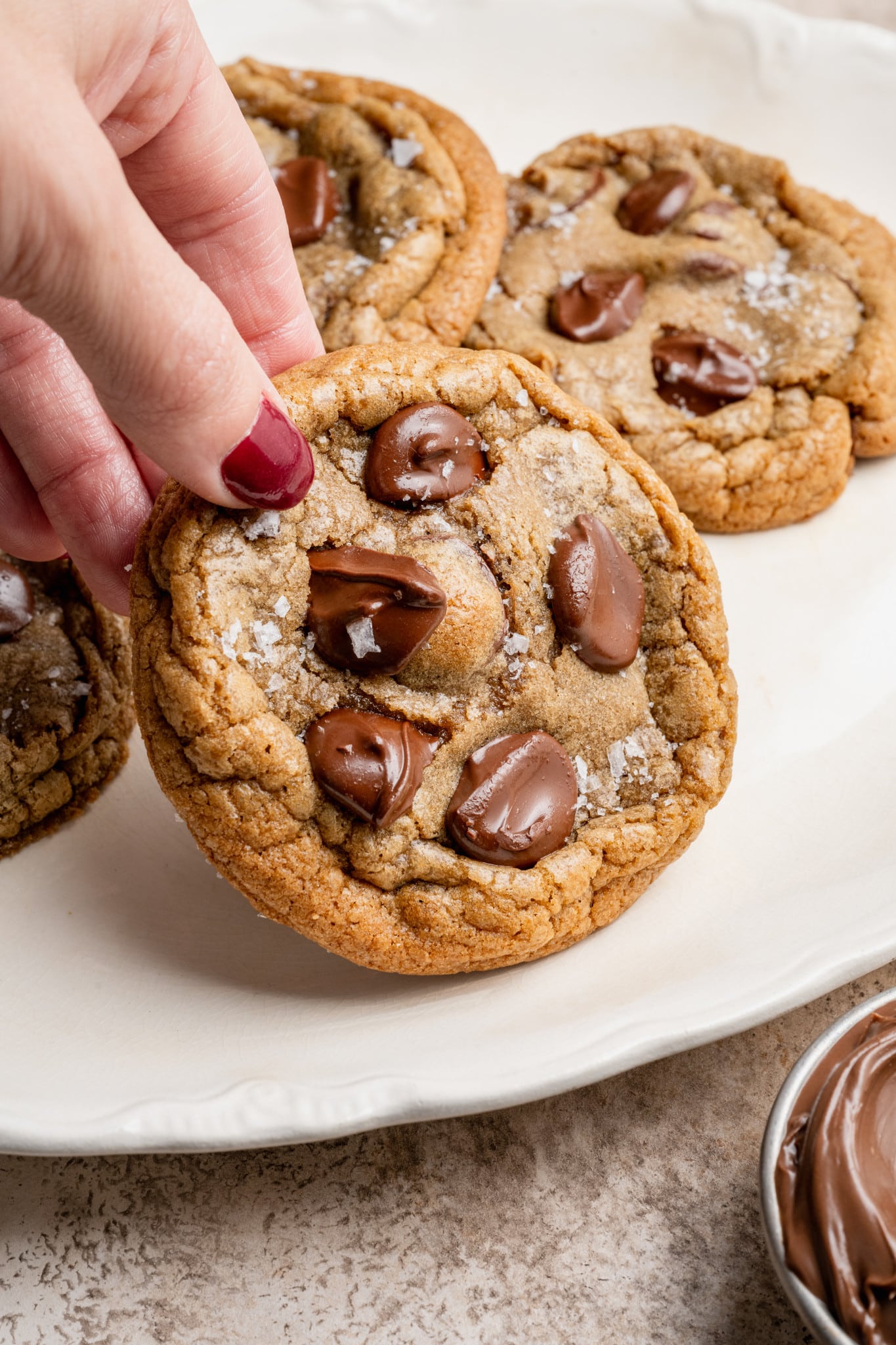 Hand holding up nutella stuffed cookie on white plate.