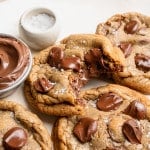 Nutella stuffed chocolate chip cookies on plate with a bite taken out of one of the cookies to show the center.