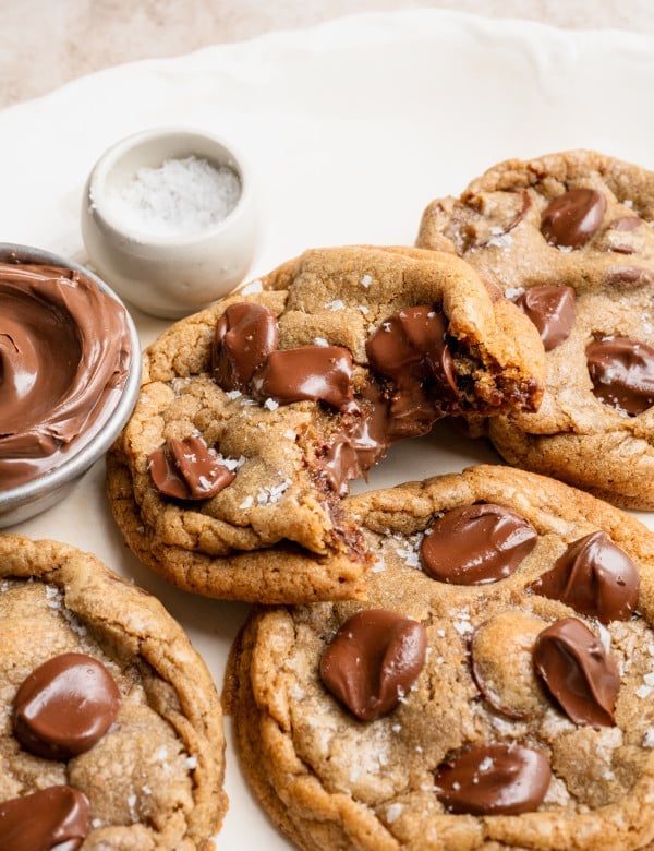 Nutella stuffed chocolate chip cookies on plate with a bite taken out of one of the cookies to show the center.