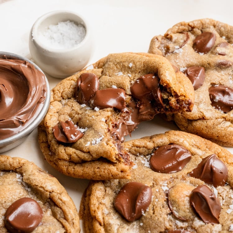 Nutella stuffed chocolate chip cookies on plate with a bite taken out of one of the cookies to show the center.