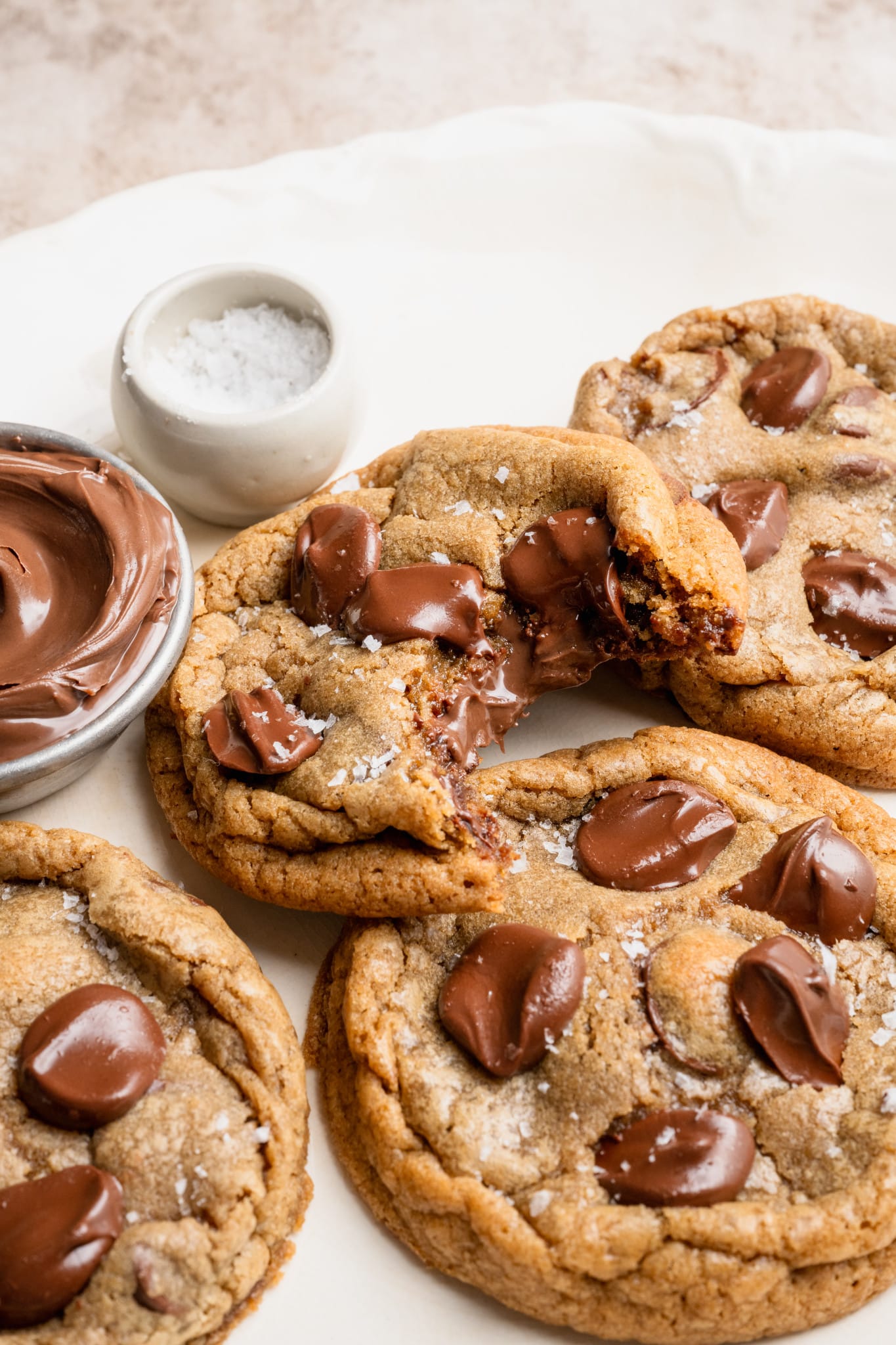Nutella stuffed chocolate chip cookies on plate with a bite taken out of one of the cookies to show the center.