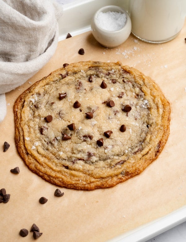 Giant single-serve thin and chewy cookie on baking tray lined with parchment paper.