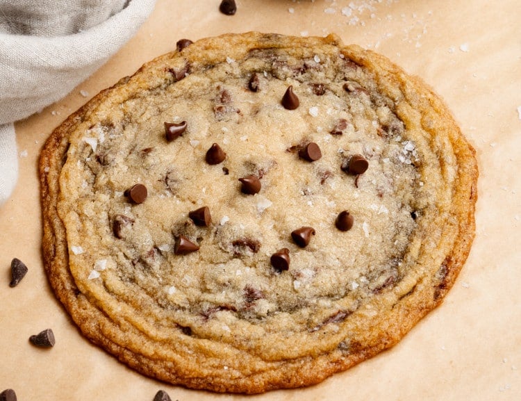 Giant single-serve thin and chewy cookie on baking tray lined with parchment paper.