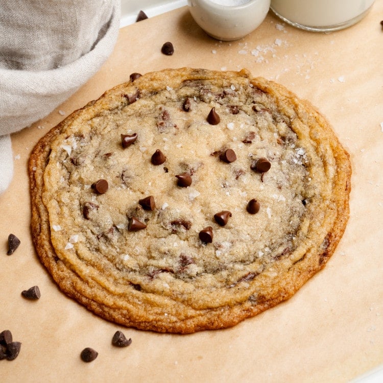 Giant single-serve thin and chewy cookie on baking tray lined with parchment paper.