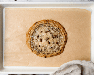 Baked single-serve thin and chewy cookie on parchment lined baking tray.