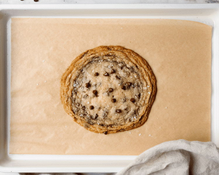 Baked single-serve thin and chewy cookie on parchment lined baking tray.