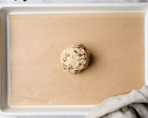 Giant ball of cookie dough shaped on cookie tray.