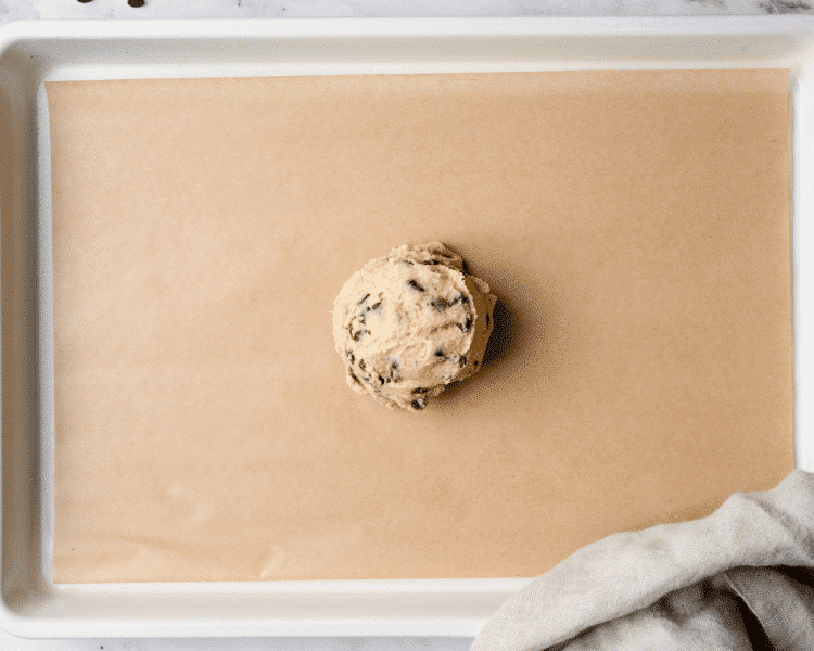 Giant ball of cookie dough shaped on cookie tray.