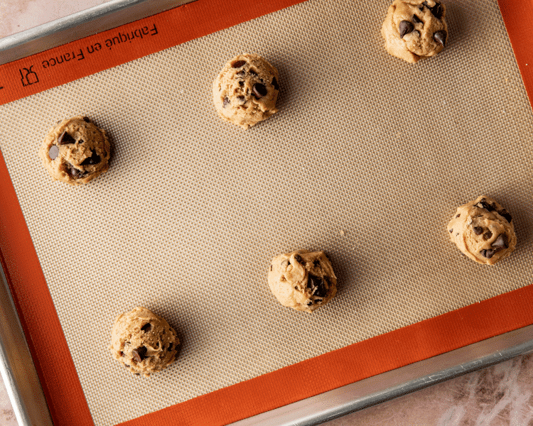 Six scoops of chocolate chip cookie dough on baking sheet.
