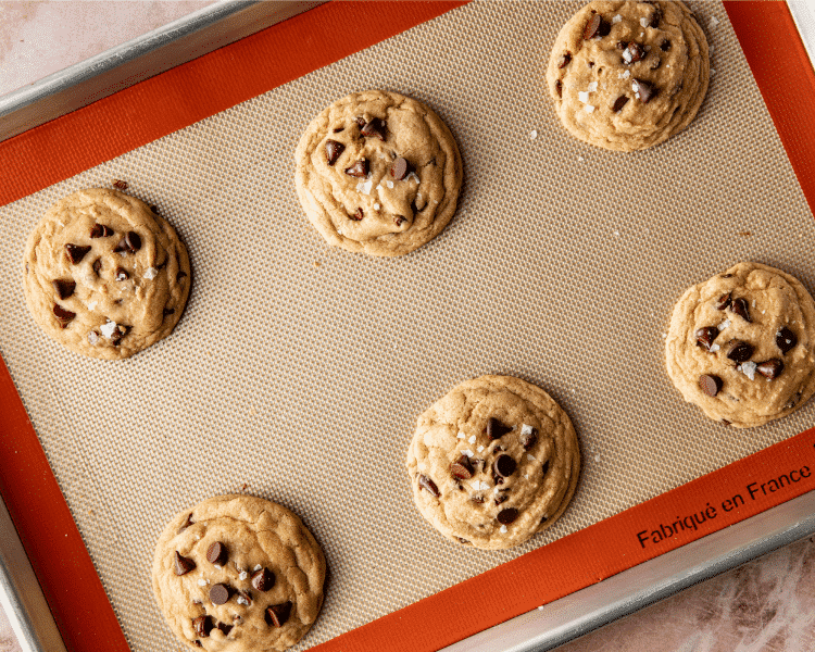 Six chocolate chip cookies baked on baking sheet.