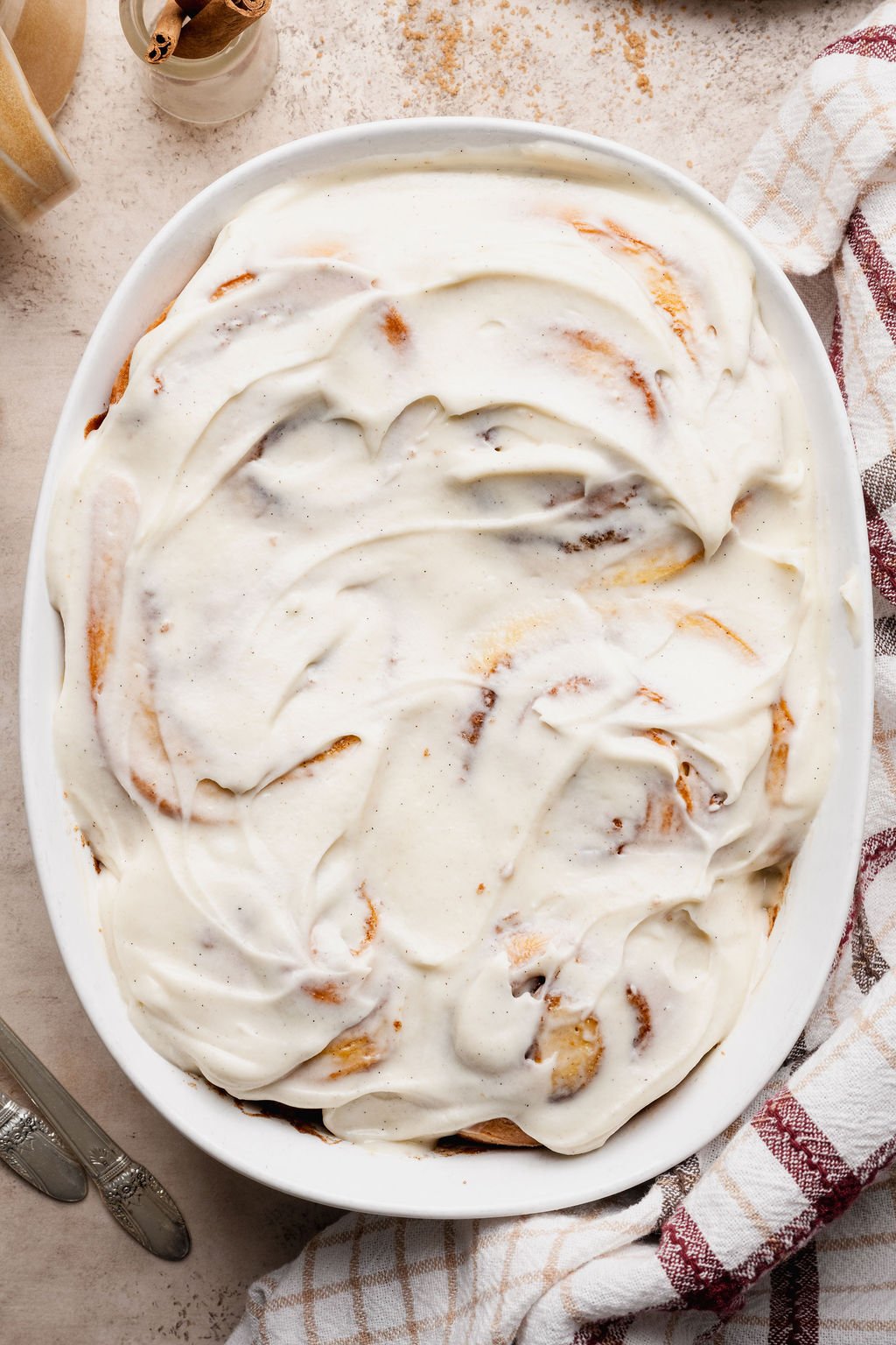 Overhead close-up of cinnamon rolls generously covered in cream cheese frosting, showing swirls of frosting texture and golden edges peeking through.