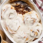 Overhead view of a baking dish with partially eaten cinnamon rolls covered in cream cheese frosting, revealing gooey cinnamon filling beneath.