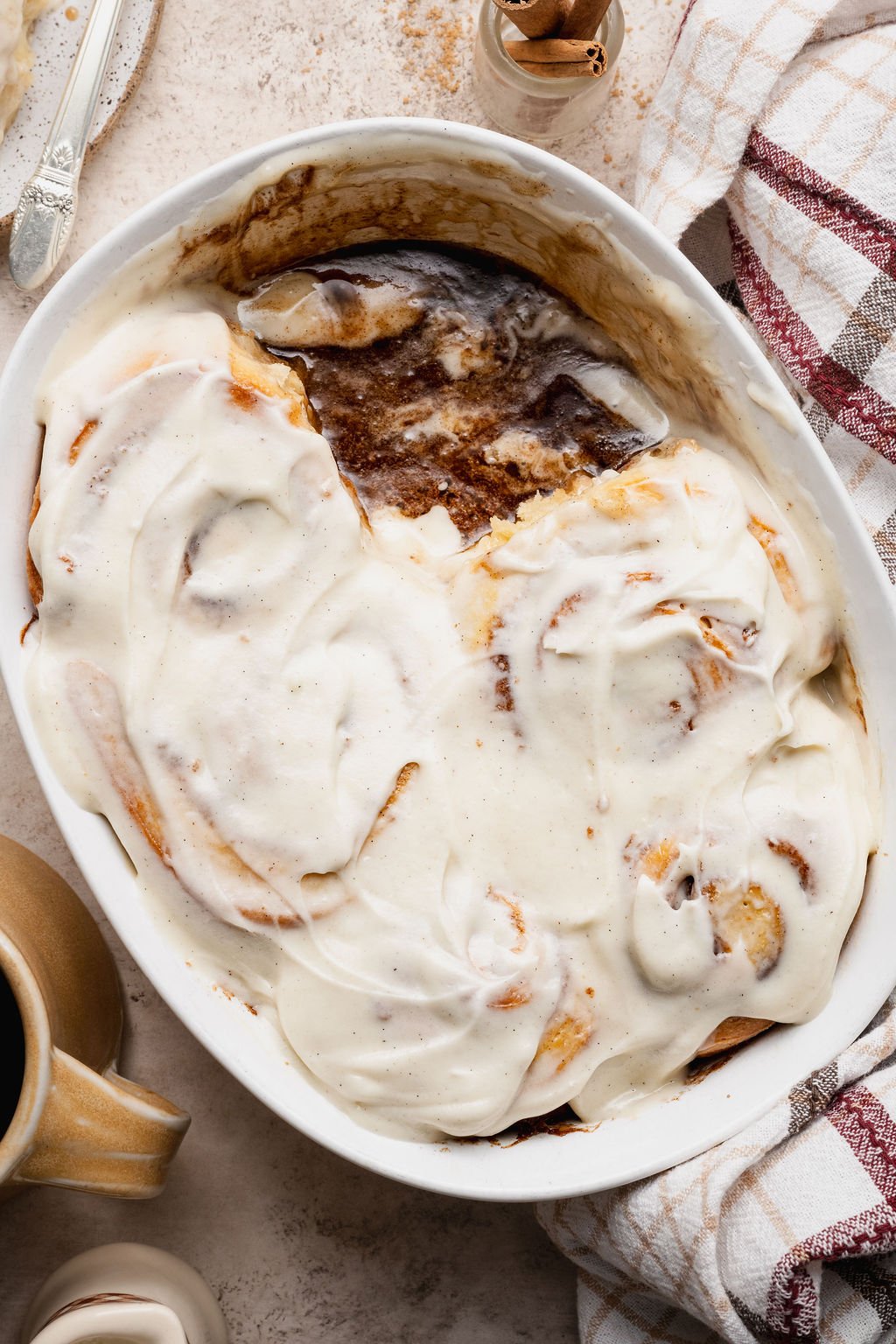 Overhead view of a baking dish with partially eaten cinnamon rolls covered in cream cheese frosting, revealing gooey cinnamon filling beneath.