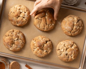Hand grabbing snickerdoodle cookie off baking sheet.