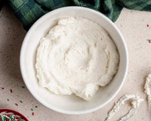 A mixing bowl filled with smooth, whipped vanilla buttercream frosting ready to spread on the cooled cookie bars.