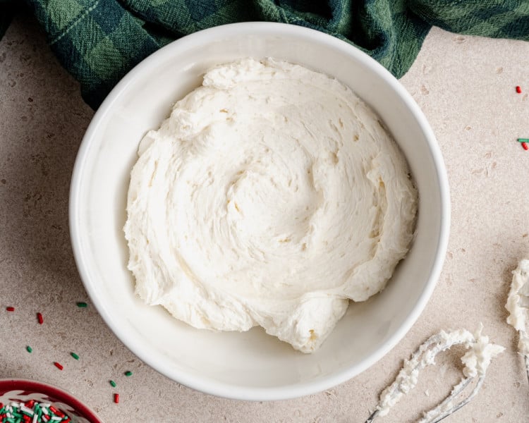 A mixing bowl filled with smooth, whipped vanilla buttercream frosting ready to spread on the cooled cookie bars.