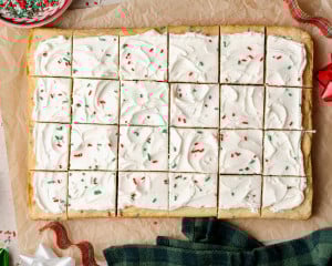 Overhead view of the finished Christmas Sugar Cookie Bars. The bars are frosted, topped with festive red, green, and white sprinkles, and sliced into even squares on a sheet of parchment paper.