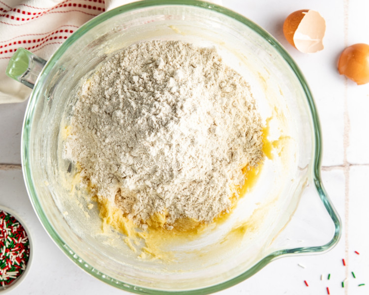 Mixing bowl with creamed wet ingredients and dry ingredients—flour, baking powder, and baking soda—added on top before combining into cookie dough.