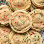 Close-up of Christmas sugar cookies with red and green sprinkles stacked on a wire rack, showing their soft, chewy texture and lightly sugared tops.