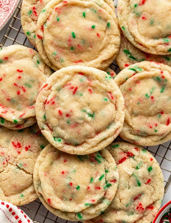 Close-up of Christmas sugar cookies with red and green sprinkles stacked on a wire rack, showing their soft, chewy texture and lightly sugared tops.