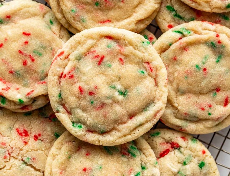Close-up of Christmas sugar cookies with red and green sprinkles stacked on a wire rack, showing their soft, chewy texture and lightly sugared tops.