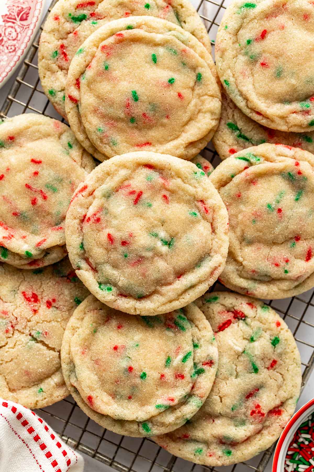 Close-up of Christmas sugar cookies with red and green sprinkles stacked on a wire rack, showing their soft, chewy texture and lightly sugared tops.