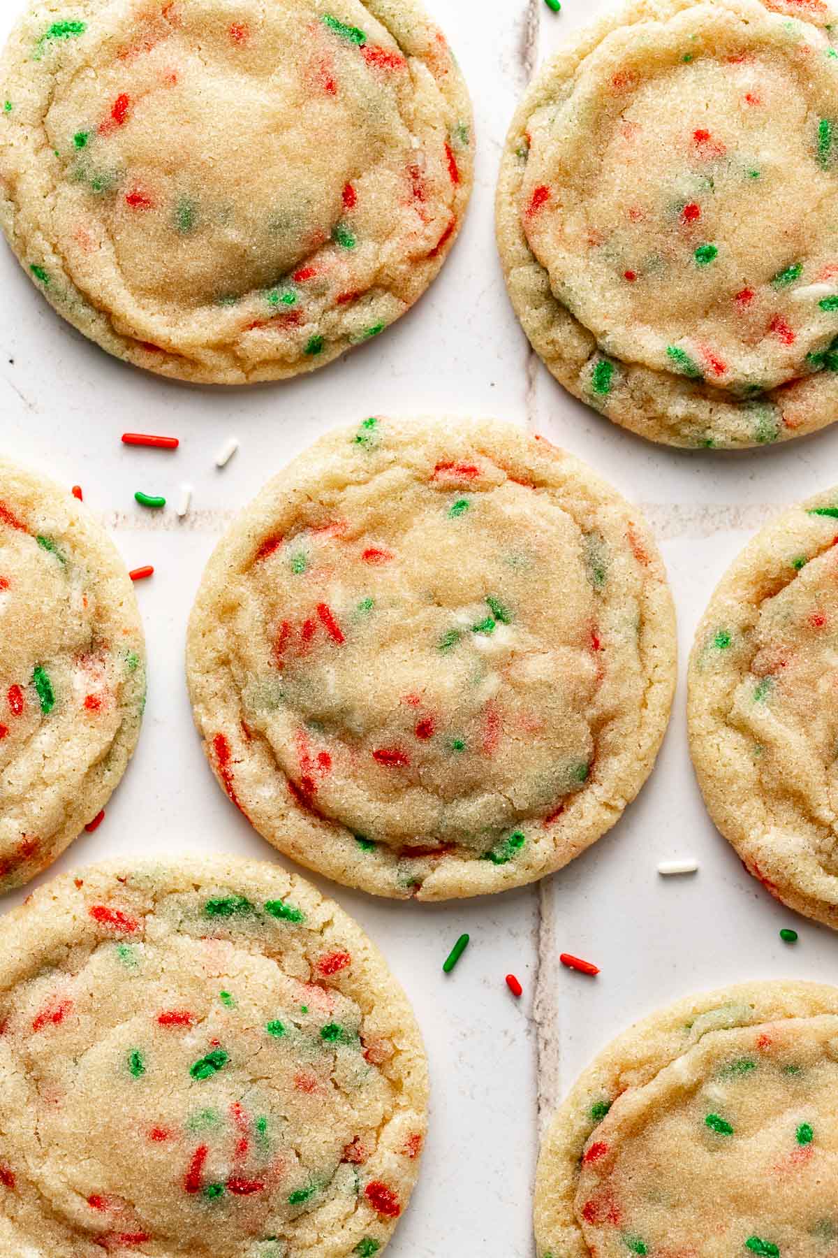 Overhead view of sugar cookies decorated with red and green sprinkles on a white surface, highlighting their crinkled edges and soft centers.