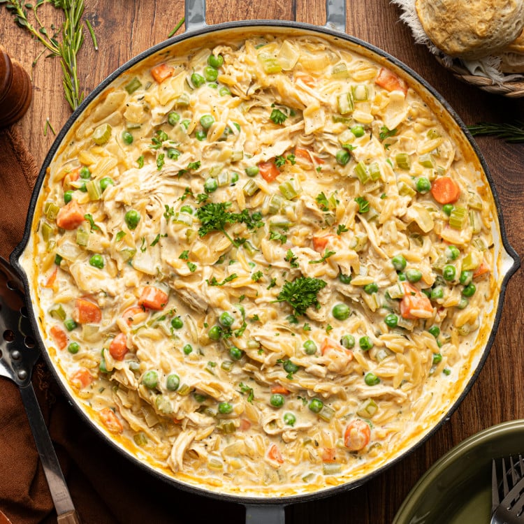 Chicken pot pie orzo cooked in a deep skillet and garnished with fresh parsley.